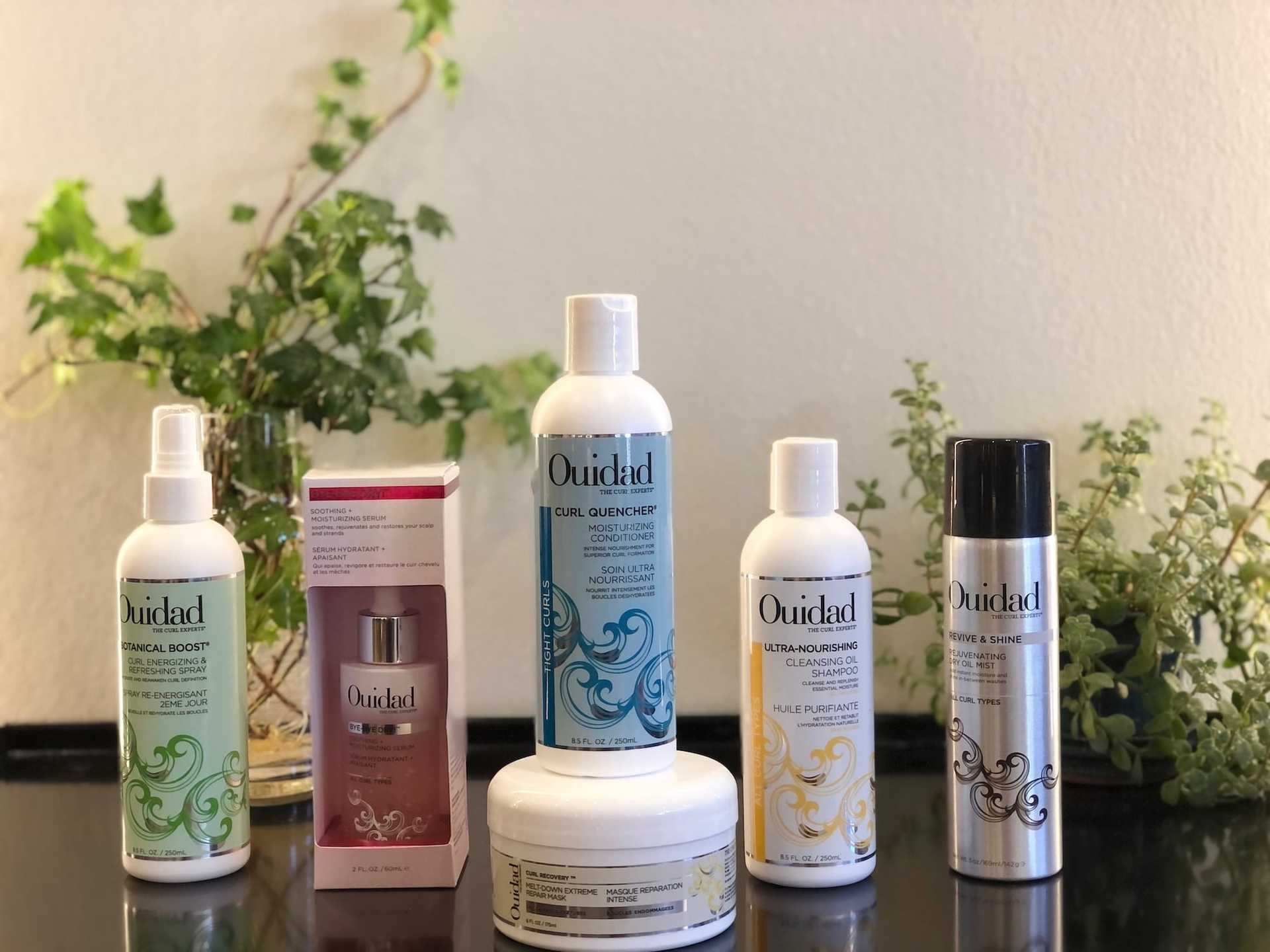 Ouidad hair products displayed on a counter with plants in the background.